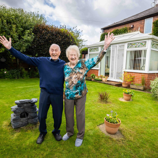 An elderly couple with their hands high on their lawn