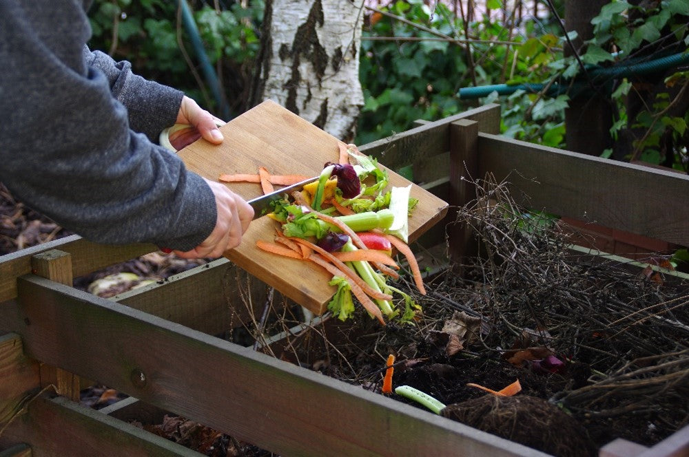 vegetable peelings being scrapped into a compost heap 