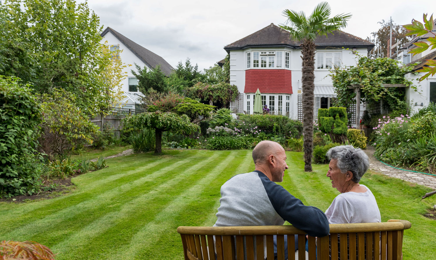 Man and woman talking on a bench in front of garden