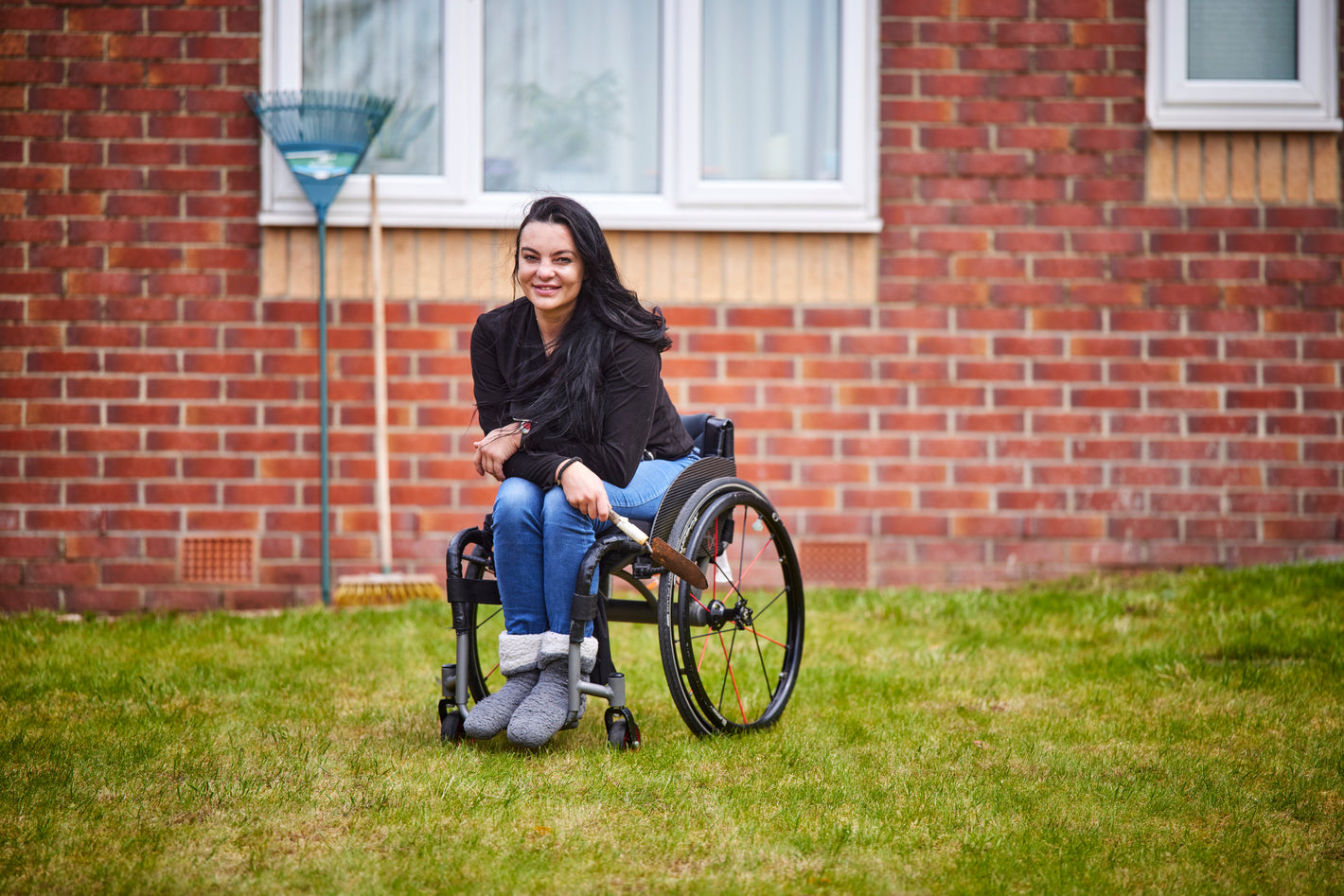lady in a wheelchair on a lawn with a rake and brush in the background