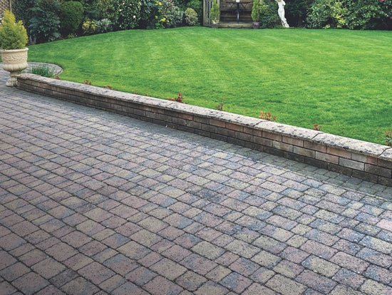 Block paved patio and a lawn separated by a small wall